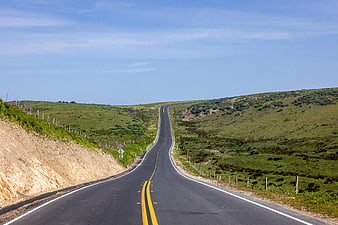 Empty asphalt road winding through green rolling hills