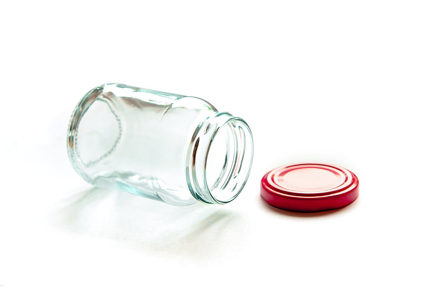 Empty glass jar with red lid on white background