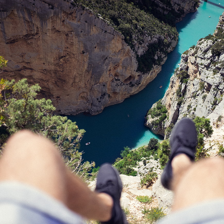 First-person view of legs dangling over a turquoise river canyon