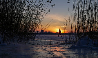 Silhouette of Person Walking on Frozen Lake at Sunset