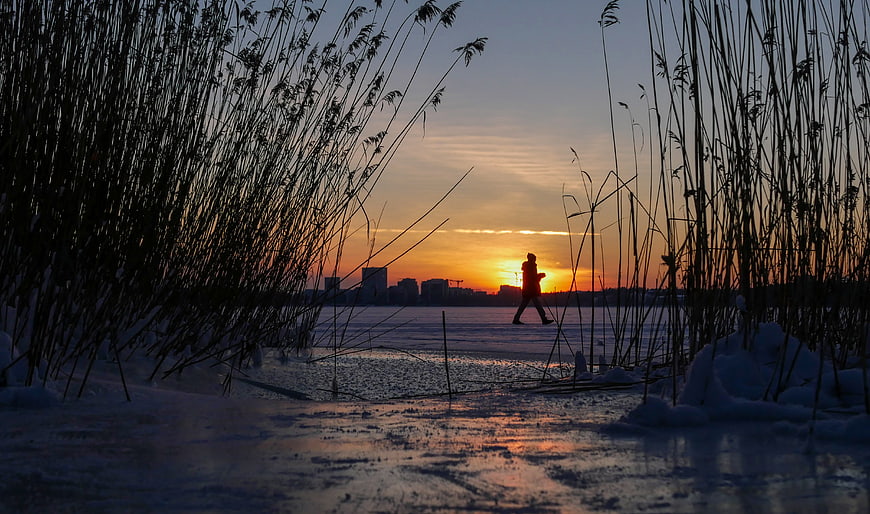 Silhouette of Person Walking on Frozen Lake at Sunset