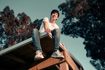 Young Man Sitting on Wooden Roof Looking Up at Sky
