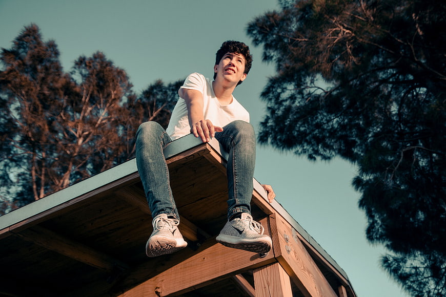 Young Man Sitting on Wooden Roof Looking Up at Sky
