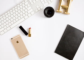 Flat lay of workspace with gold phone, lipstick, and camera lens