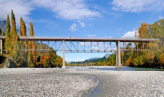 Steel Bridge Over Rocky Riverbed in Autumn Landscape