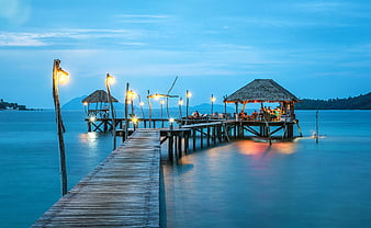 Illuminated wooden pier at twilight with thatched beach bar