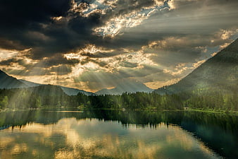 Dramatic Sun Rays Over Mountain Lake with Forest Reflection
