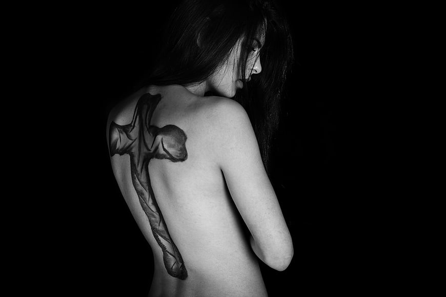 Black and white portrait of woman with cross tattoo on back