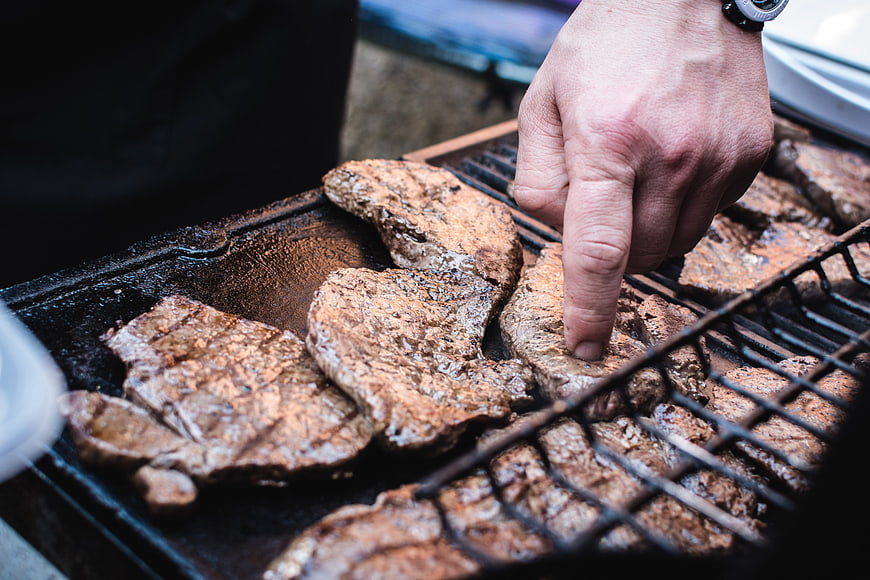 Close-up of hand checking grilled beef steaks on barbecue