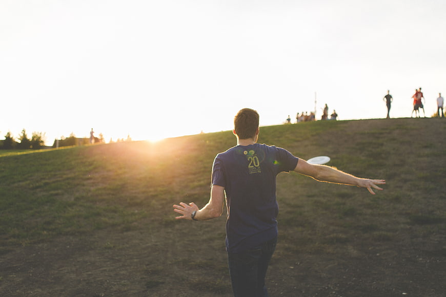 Man throwing frisbee on grassy hill at sunset