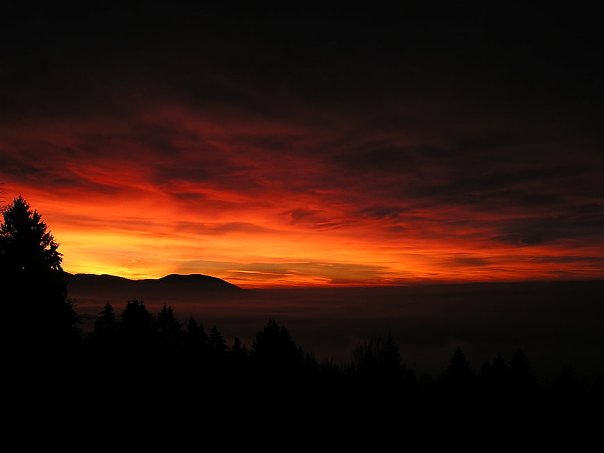 Dramatic fiery sunset over silhouetted mountain forest landscape