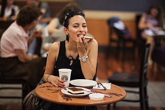 Young woman eating cookie and drinking coffee at cafe table