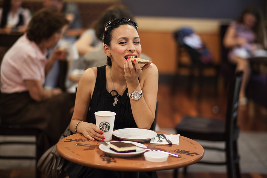 Young woman eating cookie and drinking coffee at cafe table