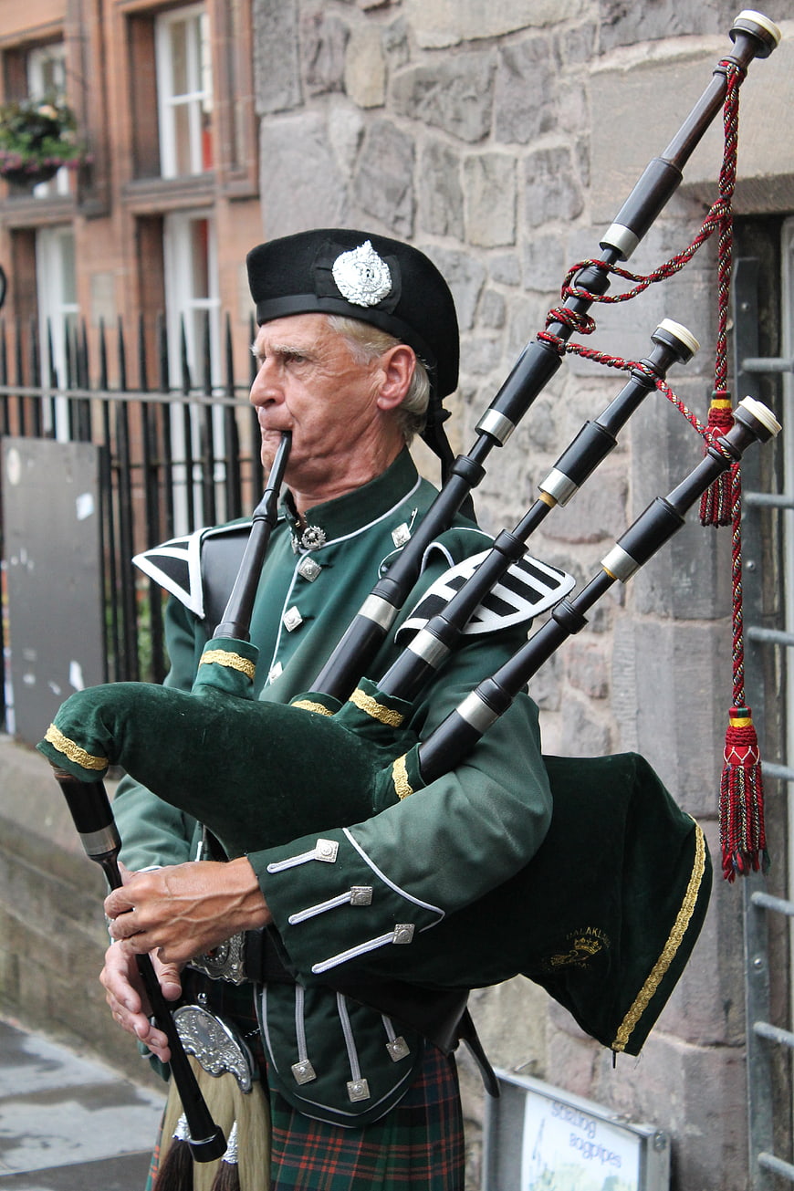 Scottish Bagpiper in Traditional Green Uniform Playing Outdoors