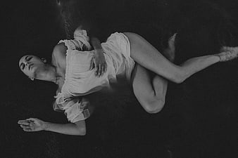 Black and white portrait of a woman in a white dress lying on a dark surface