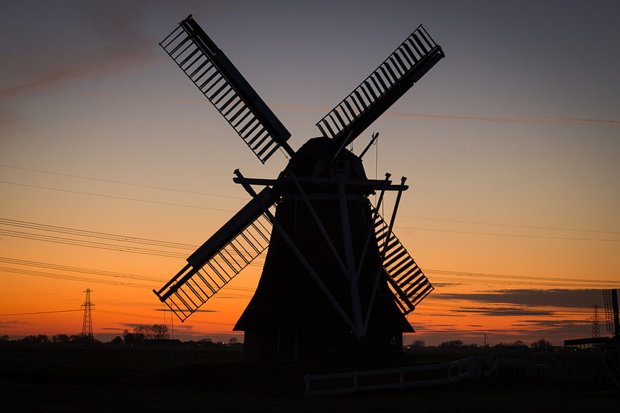 Silhouette of a traditional Dutch windmill against a vibrant orange sunset sky