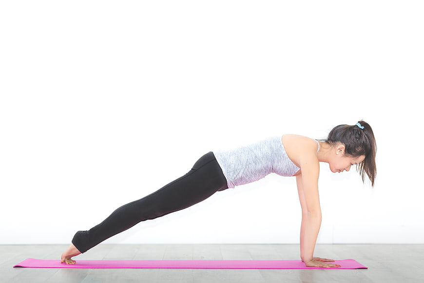 Woman doing plank exercise on pink yoga mat