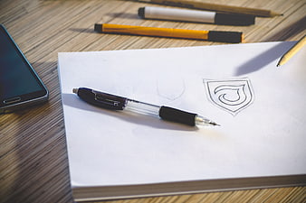 Pencil sketch of logo design on white paper with pen and smartphone