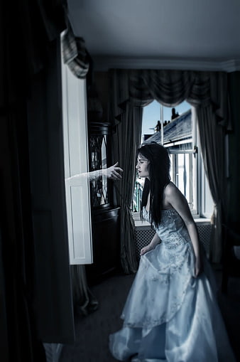 Woman in white dress reaching toward ghostly hand in dark room