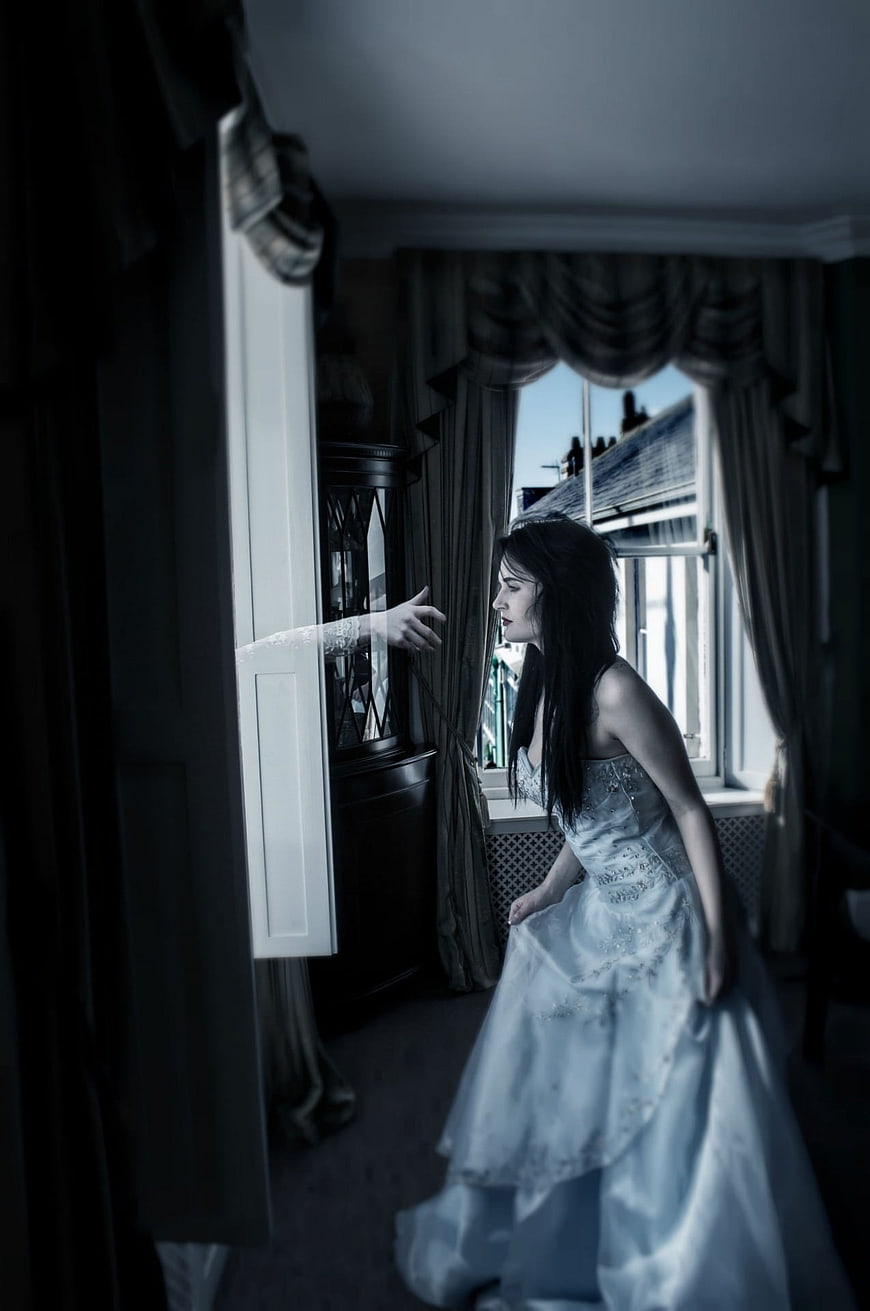 Woman in white dress reaching toward ghostly hand in dark room