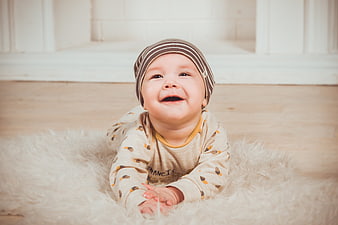 Happy baby crawling on fluffy rug in striped hat
