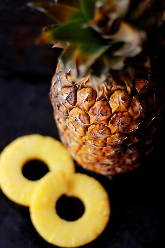 Whole pineapple with sliced rings on dark background