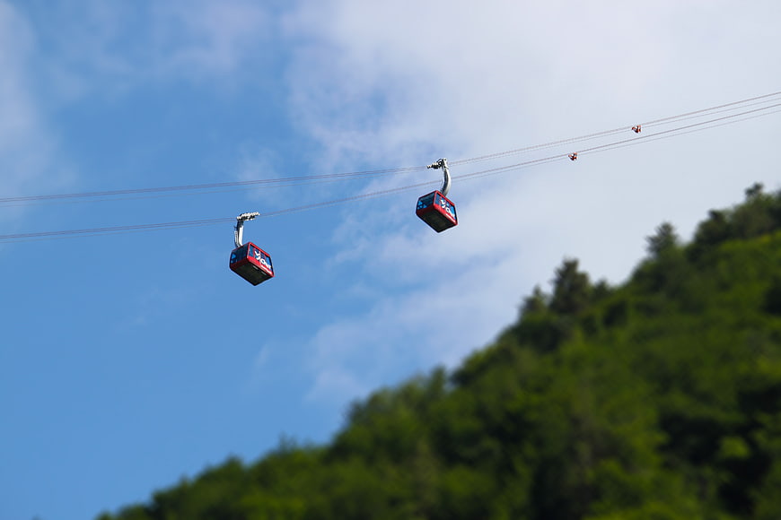 Red Cable Cars Ascending Green Mountain Against Blue Sky