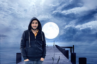 Man in Hoodie Standing on Pier with Giant Moon
