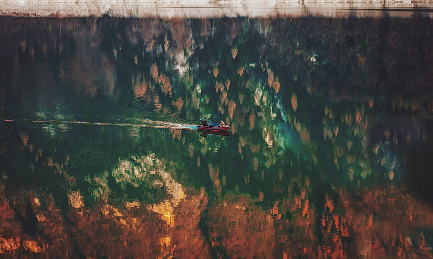 Aerial view of boat on river with autumn forest reflection