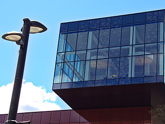 Modern glass office building with street lamp against blue sky