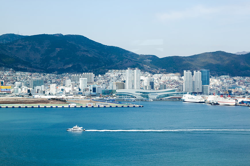 Wide view of coastal city harbor with ferry and mountains