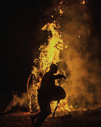 Silhouette of man dancing near large bonfire at night