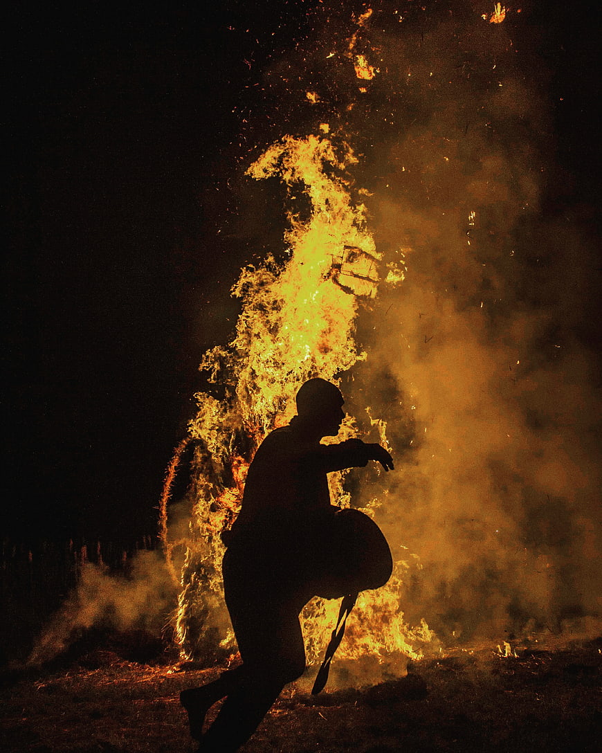Silhouette of man dancing near large bonfire at night