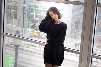 Woman in black sweater posing by large window