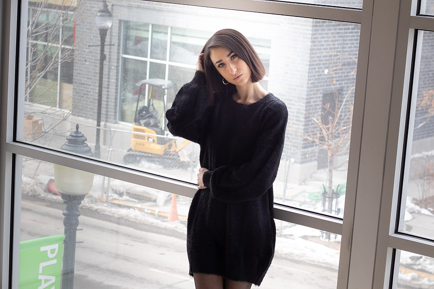 Woman in black sweater posing by large window