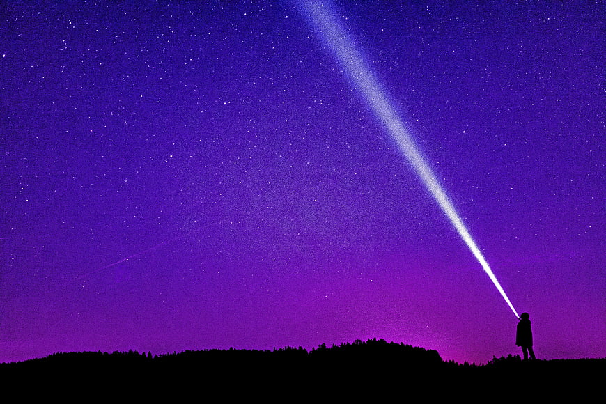 Silhouette of Person Shining Flashlight into Purple Starry Night Sky
