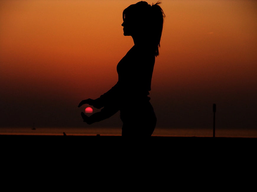 Silhouette of Woman Holding Sun at Sunset