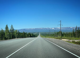 Long straight highway stretching to snow-capped mountains under blue sky
