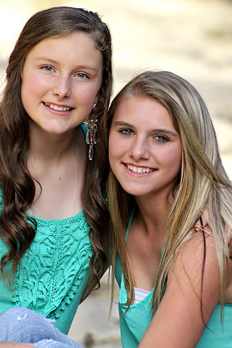 Two smiling teenage girls in matching teal tops outdoors