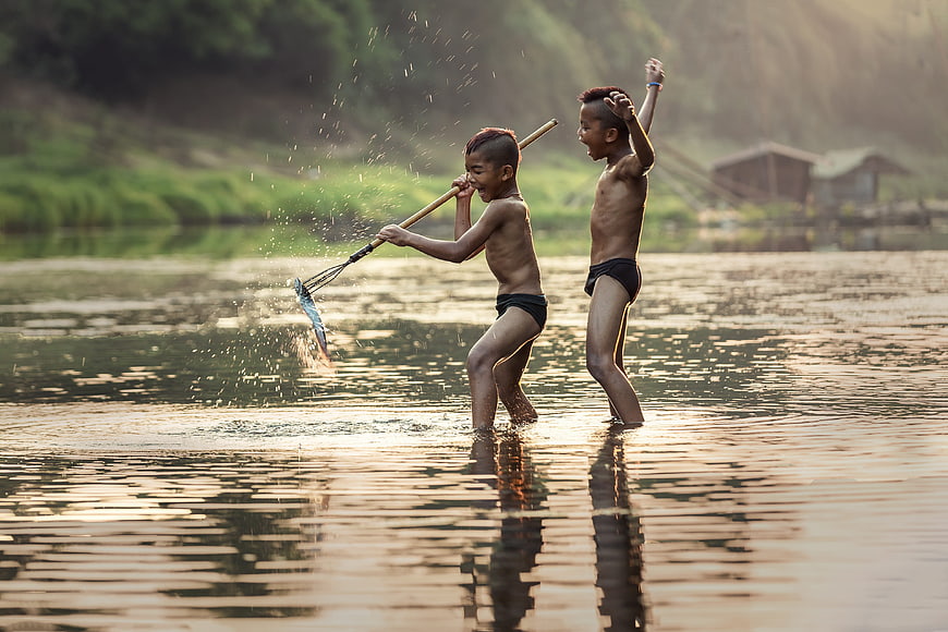 Two boys playing with a fishing net in a river at sunset