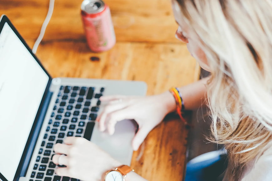 Woman typing on laptop at wooden desk with drink
