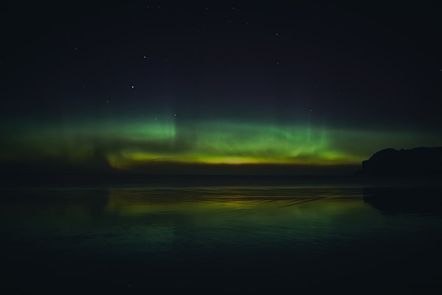 Green Aurora Borealis Reflecting on Calm Ocean Water at Night