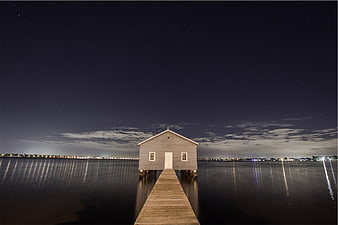 Solitary boathouse on wooden pier at night with starry sky