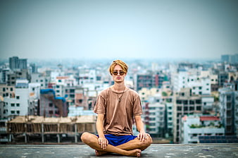 Young Man Meditating on Rooftop with City Skyline Background