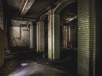 Dark abandoned tiled basement with pillars and pipes
