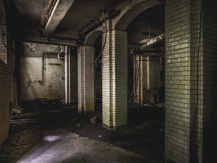 Dark abandoned tiled basement with pillars and pipes