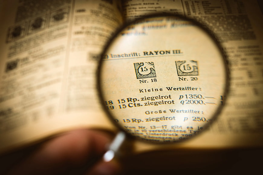 Magnifying glass inspecting vintage philatelic catalog text