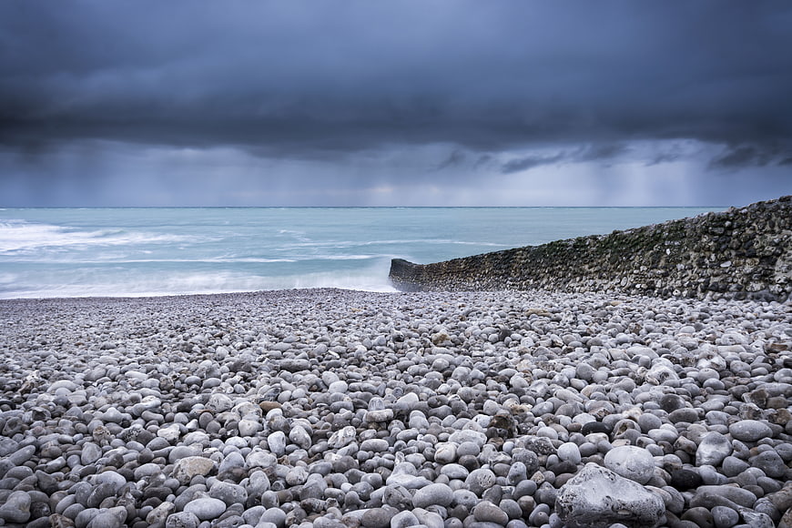 Stormy Pebble Beach with Rocky Breakwater and Dark Clouds