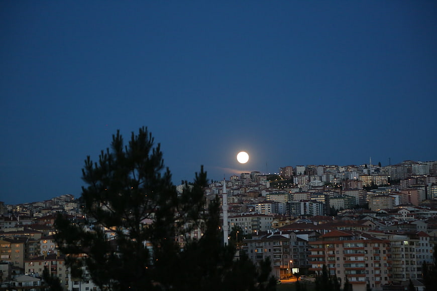Full moon rising over a densely populated cityscape at dusk