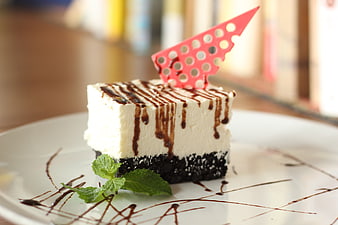 Chocolate Drizzled Cheesecake Slice With Mint Garnish On White Plate
